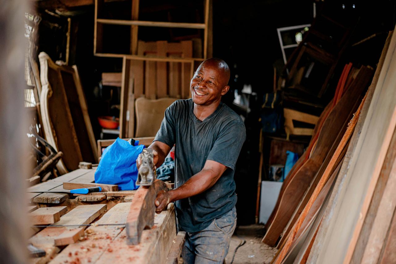 a man smiles as he works on a piece of wood