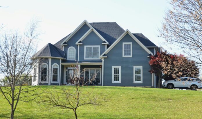 A large blue house sits on a grassy hill.