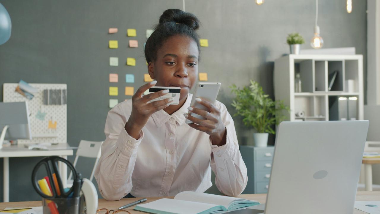 Woman holding credit card and phone at desk.